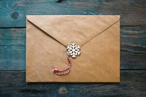 A brown paper envelope sealed with a twine and wooden snowflake ornament, placed on a blue wooden surface.