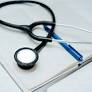 A stethoscope, blue pen, and clipboard with paper are arranged on a white surface.