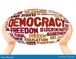 Two hands hold an oval shape filled with words like "Democracy," "Freedom," "Human Rights," "Tolerance," and "Education" in various fonts and colors.