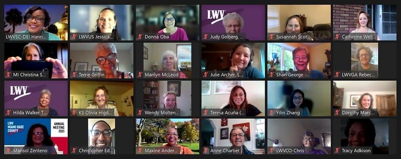 A screenshot of a virtual meeting with 25 people smiling, some holding up signs or notebooks, each shown in individual video call windows against various backgrounds.